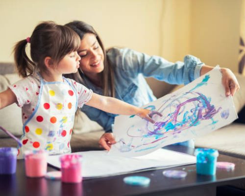 A young mother and her cute little daughter painting with colorful paints and having fun at home.