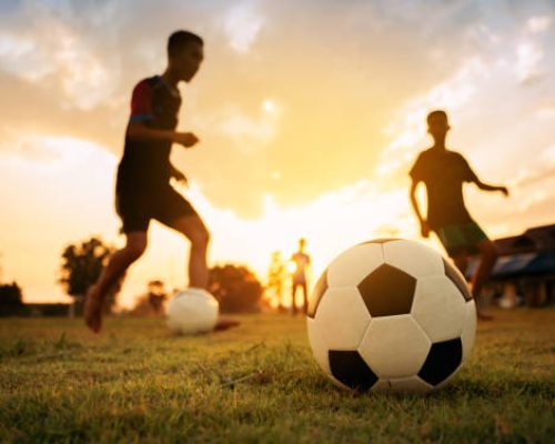 action sport outdoors of a group of kids having fun playing soccer football on the dirt field.