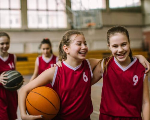 Cute teenage girls, smiling and hugging after basketball match, happy after winning the game